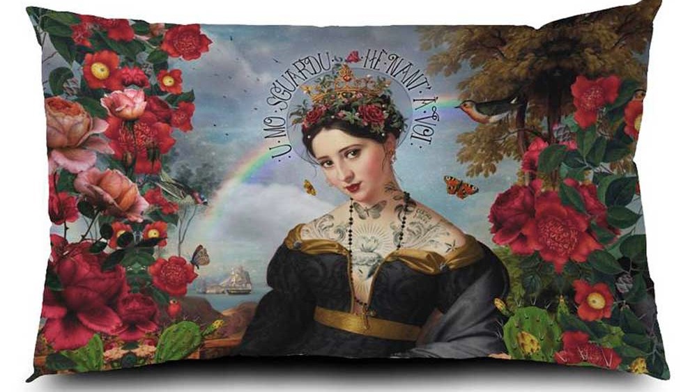 Voglio Bene Samtkissen Santa di U Niolu 40x65 – kunstvolles Porträt einer gekrönten Frau mit Tattoos, umgeben von üppigen Blumen, Schmetterlingen, Vögeln und Regenbogen, im romantischen Landschaftshintergrund.