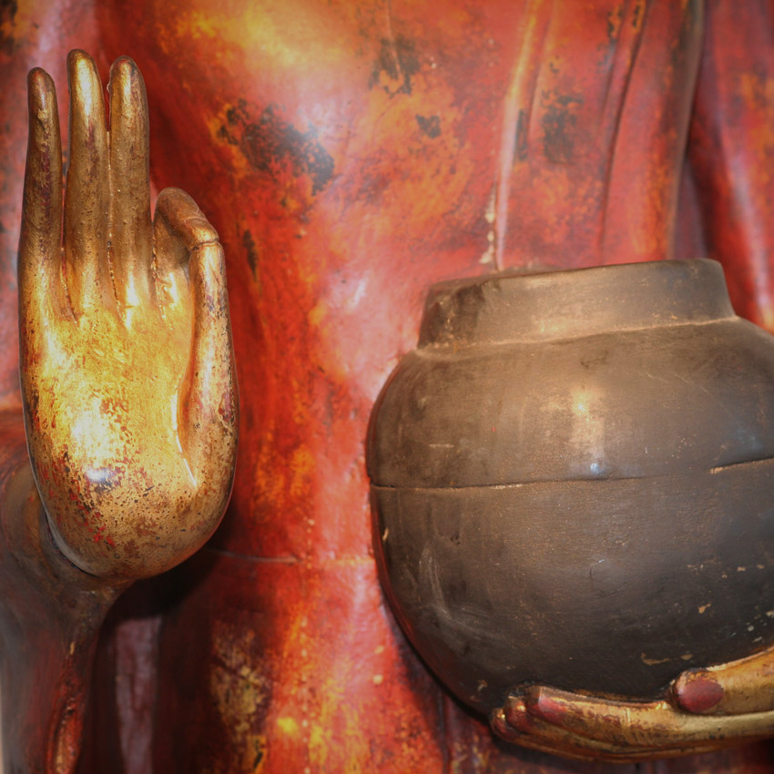 Detailansicht der Hand und Opferschale eines großen roten Buddha, vergoldete Geste der Großzügigkeit vor roter Patina, Symbol der Achtsamkeit.