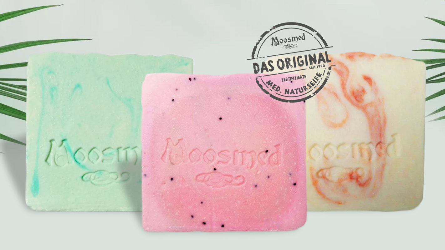 Drei bunte Moosmed Naturseifen in Grün, Rosa und Creme mit Logo-Prägung. Handgemachte, zertifizierte medizinische Seifen – pflegend, natürlich und nachhaltig.