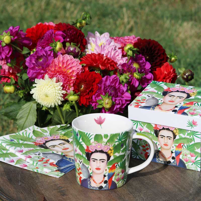 Porzellantasse Coyoacán von PPD mit Frida-Kahlo-Motiv, tropischen Blättern und Papagei. Geschenkbox und Servietten im passenden Design, dekoriert mit bunten Dahlien im Garten.