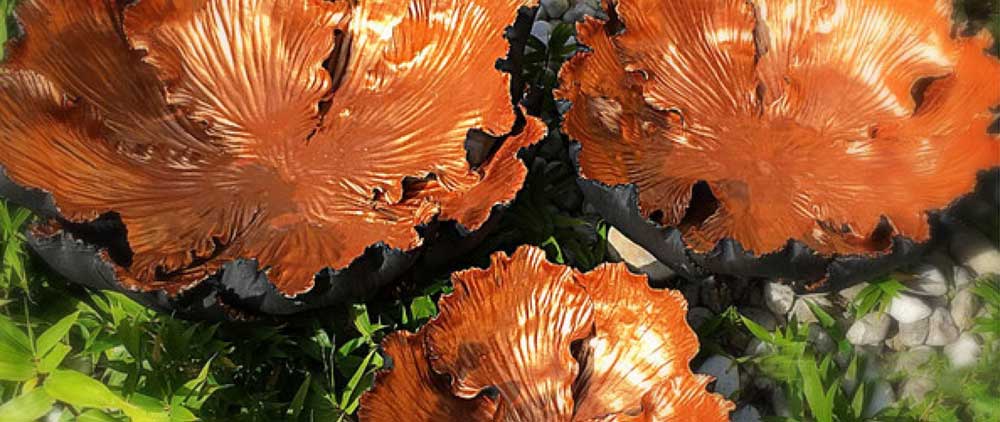 Handgefertigte Keramikschalen im Thai Design mit organischer Blattform und glänzender Kupferoptik, dekorativ im Garten zwischen grünen Pflanzen arrangiert.