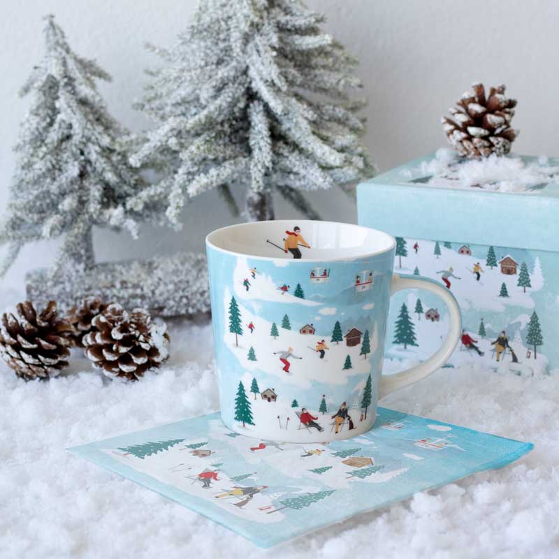 PPD Trend Mug "St. Moritz" Winterliche Porzellantasse von PPD mit Skifahrer-Motiv im Schnee, arrangiert mit passender Geschenkbox, Tannenzapfen und Schneedekoration – stimmungsvolles Winterdesign.