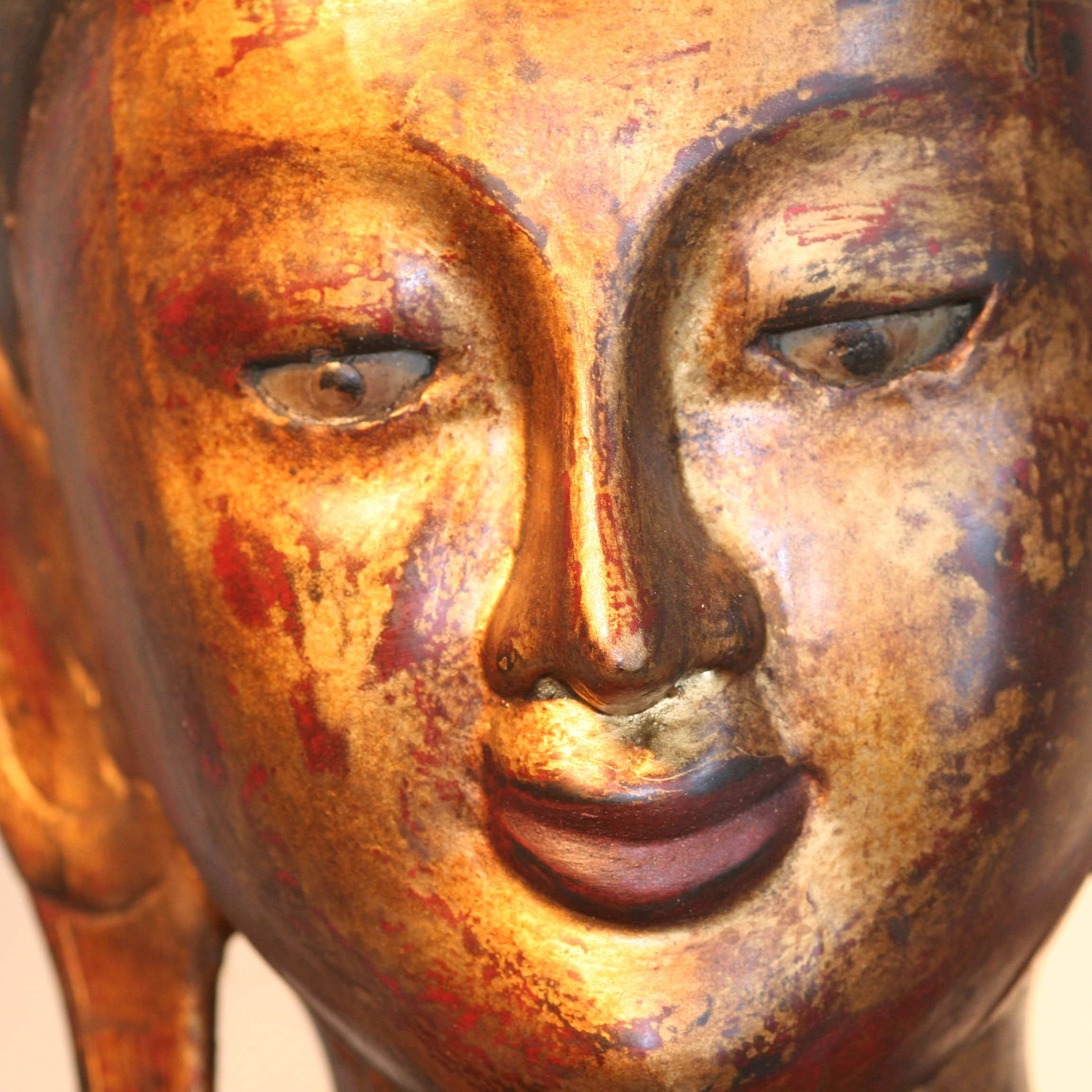Detailansicht des Gesichts eines großen roten Buddha mit Opferschale, vergoldete Oberfläche, sanfter Ausdruck und feine Handbemalung.