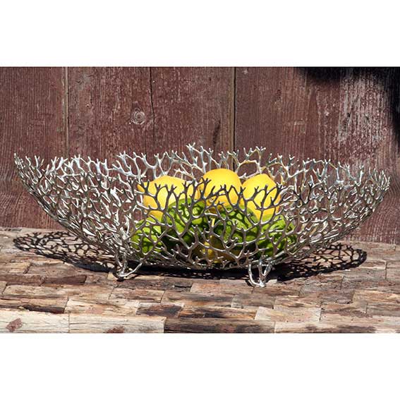 Hochwertige Zinnschale von Loyfar in filigraner Korallenoptik, dekorativ mit Zitronen und Limetten gefüllt, auf rustikalem Holztisch vor Holzrückwand.