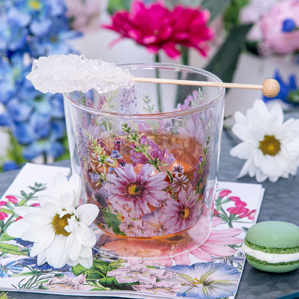 PPD Teeglas mit floralen Motiven in Rosa und Grün, dekoriert mit Blüten, einem Zucker-Stick und Macaron – stilvolle Frühlingsdeko für den Teegenuss