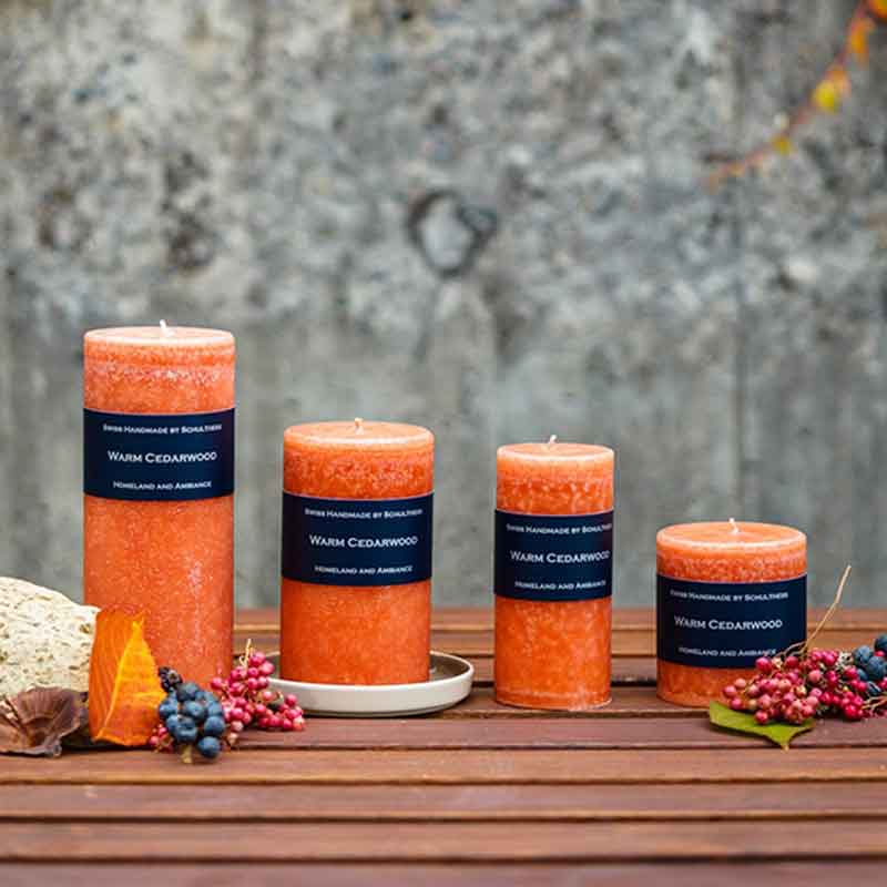Vier Schulthess Duftkerzen Warm Cedarwood aus der Kollektion Homeland and Ambiance in verschiedenen Größen, dekoriert mit Herbstblättern, Beeren und Holz auf einem Tisch – edle Duftwelt mit warmem Zedernholz-Aroma.