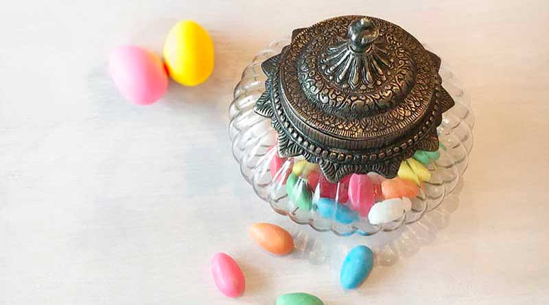 Glasbonbonniere im Antiklook mit verziertem Metalldeckel, gefüllt mit bunten Zuckermandeln. Stilvolles Aufbewahrungsglas für Süßigkeiten oder Dekoration im Vintage-Stil.